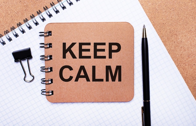 On a wooden background notepad, black pen, paper clip and brown notepad with the text KEEP CALM. Business concept