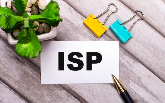 On a wooden background, a white card with the text ISP Internet Service Provider, yellow and green paper clips and a plant in a pot. View from above