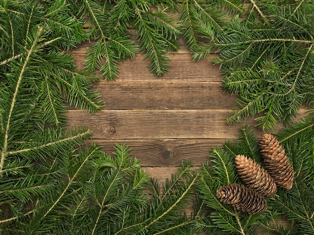 Wooden background with fir branches and cones on the edge of the frame