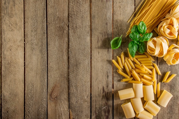 Wooden background with italian pasta and basil