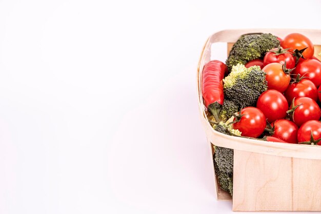 Photo a wooden basket filled with cherry tomatoes red hot peppers and pieces of raw broccoli