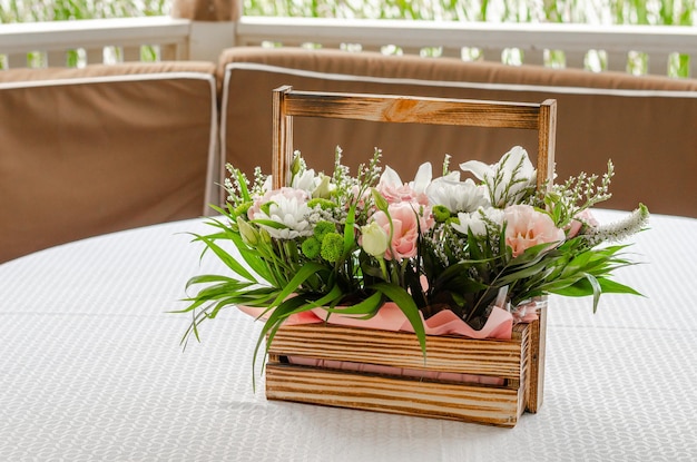 Wooden basket with a bouquet of flowers on a white tablecloth