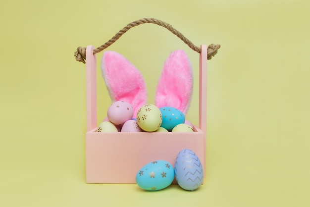 着色された卵とピンクのウサギの耳イースター コンセプト木製バスケット