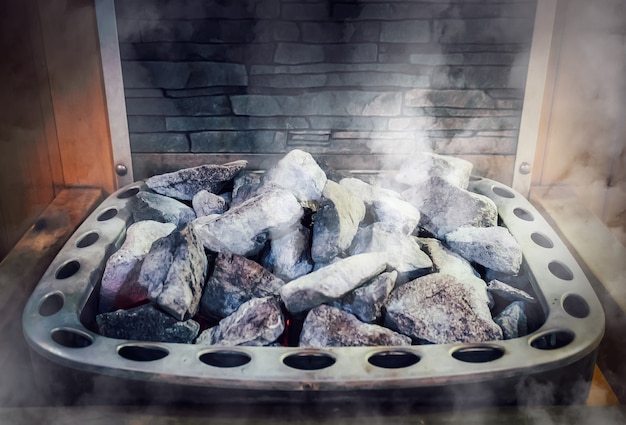 Wooden Bathhouse with a heating pot filled with stones, close up. Wooden sauna interior with equipment.