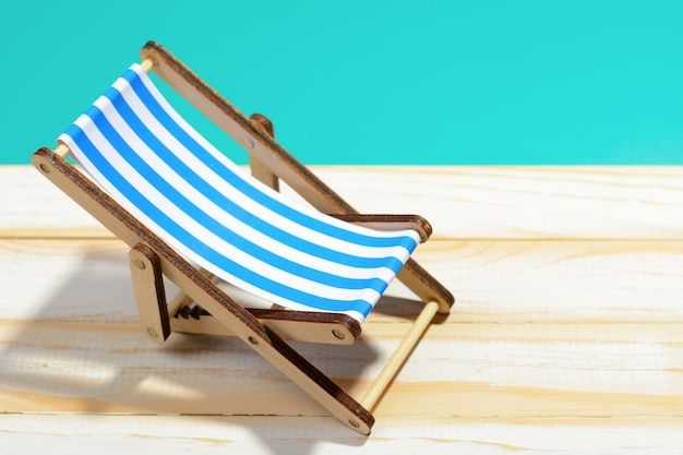 Wooden beach chair on wooden surface and blue background.