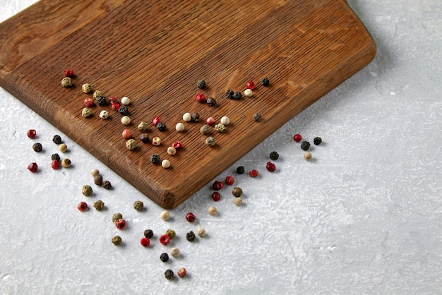 Photo wooden beige cutting board with scattered multicolored peppercorn peas on a gray stone countertop