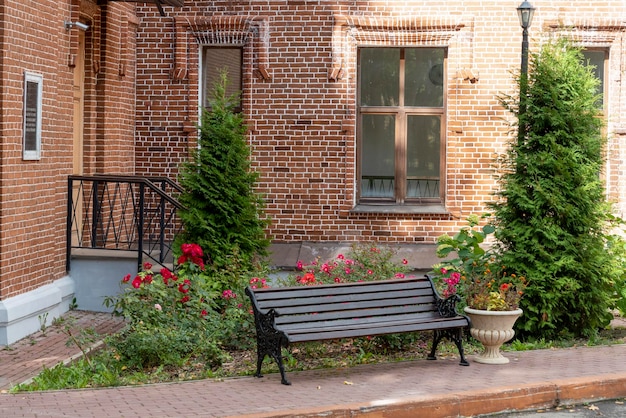 Wooden bench on the background of a brick house with flowers and trees