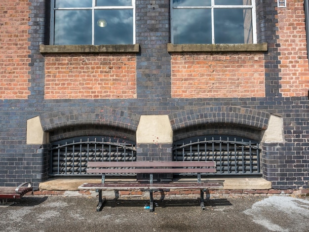 Wooden bench at front of classic old brick building under outdoor summer sunlight