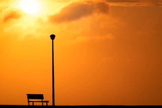 赤い夕日と明るい太陽に対する木製のベンチと街灯