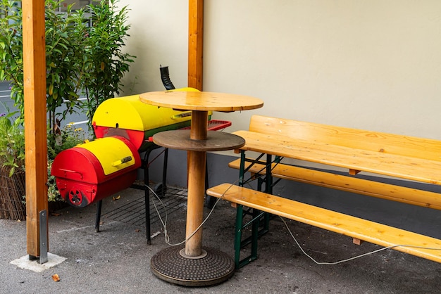 A wooden bench with a table and a bright yellow smoke grill next to the wall of the house