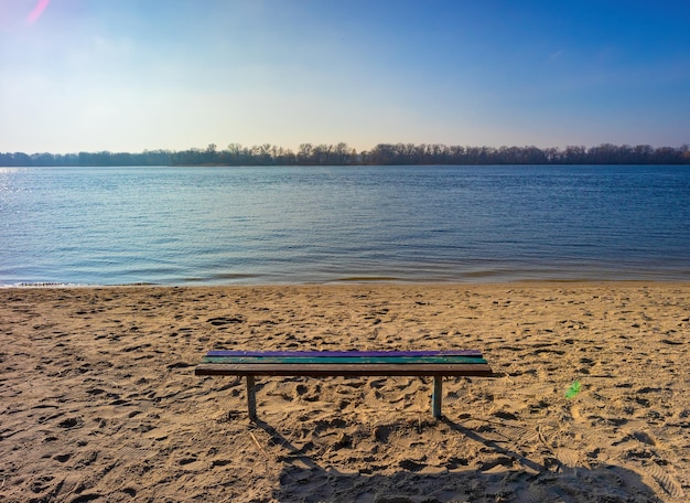 A wooden bench without people on the river bank on a sunny day