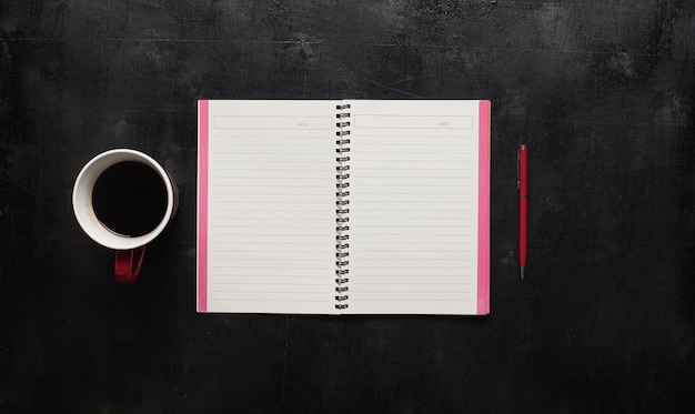 Wooden black office desk table with notebook, pen and cup of coffee