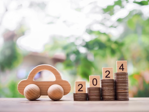 Wooden black with number 2024 on stack of coins and wooden toy car The concept of saving money for car in new year 2024