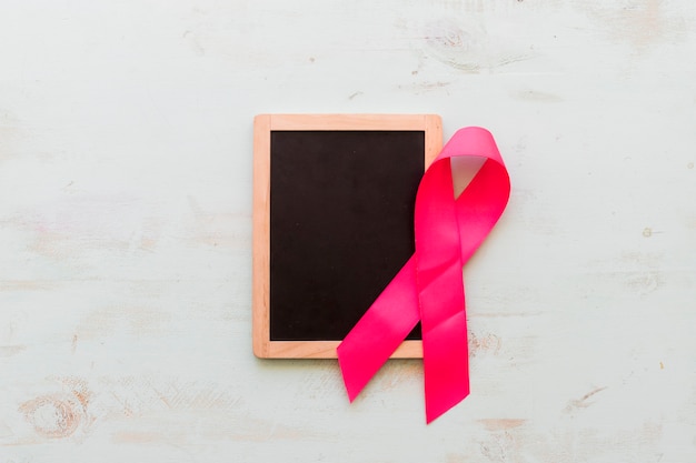 Photo wooden blank slate with pink awareness ribbon on an old background