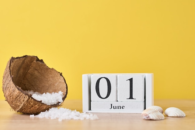 Календарь деревянных блоков с датой 1 июня и кокосом с морской солью на желтом фоне. концепция летних каникул