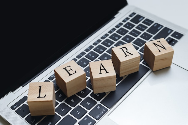 ノートパソコンに「LEARN」と書かれた木製のブロックキューブ。教育と学習のオンライン概念。