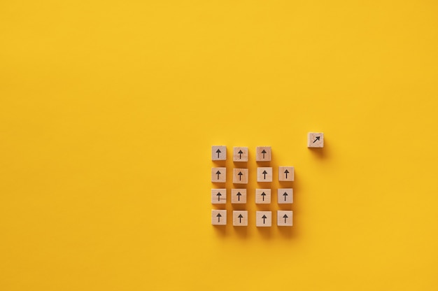 Wooden block with arrow on it separating from a group of other blocks in a conceptual image of vision and determination