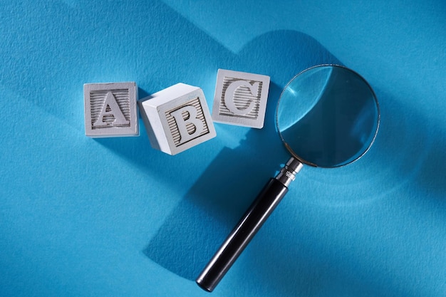 Wooden block with letter abc and magnifying glass on blue background