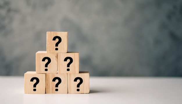 Wooden block with question mark on white table against blank wall symbolizing uncertainty and searc