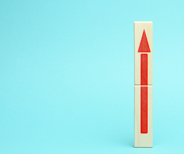 Wooden block with an upward arrow on a bluee surface, the process of growth and achievement of goals, rising prices, copy space