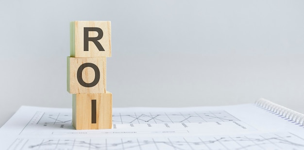 ROI-頭字語-投資収益率という言葉が書かれた木製のブロック。 ROIの木製ブロックは紙の灰色の背景にあります。ビジネスコンセプト。右側のテキスト用のスペース。正面図。