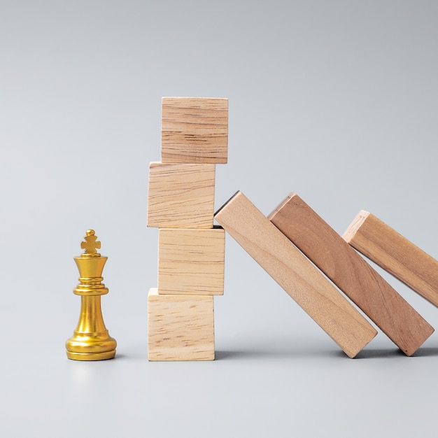 Wooden Blocks or Dominoes falling to golden Chess King figure. Business, Risk Management, Solution, economic regression, Insurance