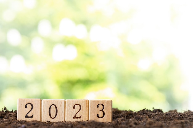 Wooden blocks lie on a wooden table against the backdrop of a summer garden and create the word 2023