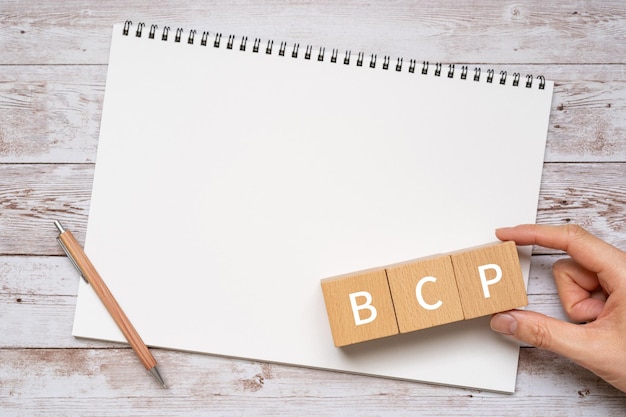 Wooden blocks with BCP text of concept, a pen, a notebook, and a hand.