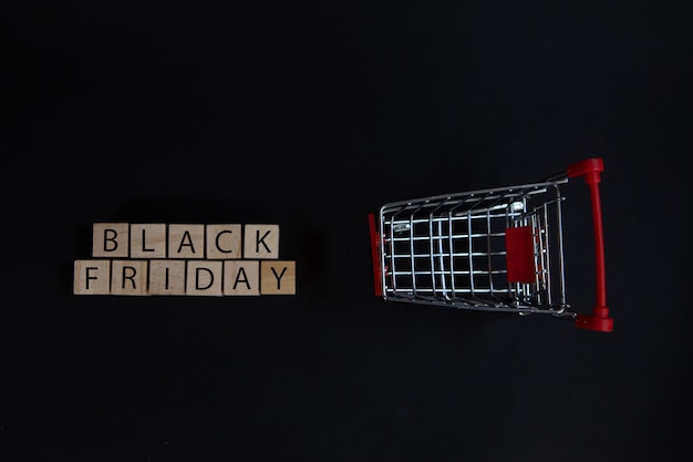 Photo wooden blocks with the black friday sign next to a supermarket cart