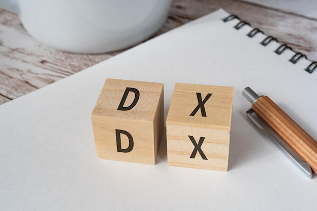 Wooden blocks with DX text of concept, a pen, a sketchbook, and a cup.