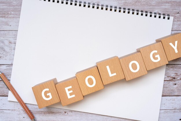 Wooden blocks with GEOLOGY text of concept, a pen, and a notebook.