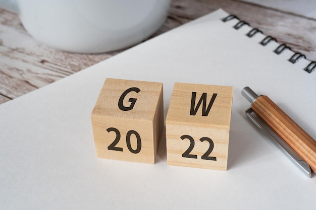 Wooden blocks with GW and 2022 text of concept, a pen, a notebook, and a cup.