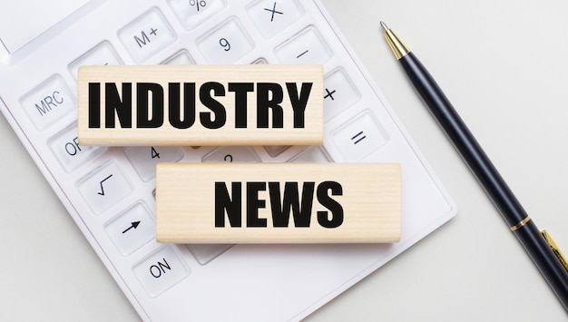 Wooden blocks with the INDUSTRY NEWS lie on a light background on a white calculator. Nearby is a black handle. Business concept