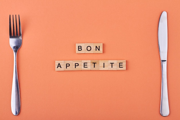 Wooden blocks with inscription Bon appetit and cutlery on color background