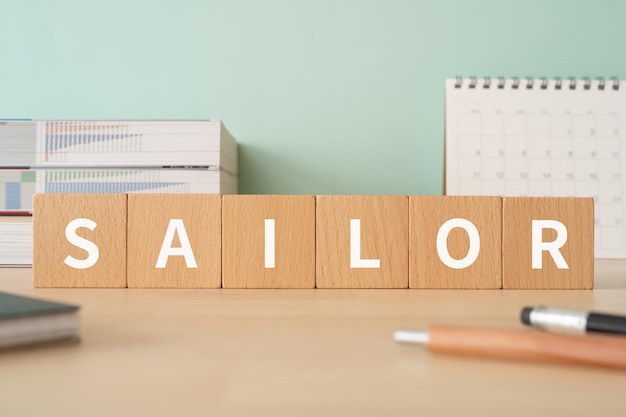 Wooden blocks with SAILOR text of concept, pens, notebooks, and books.