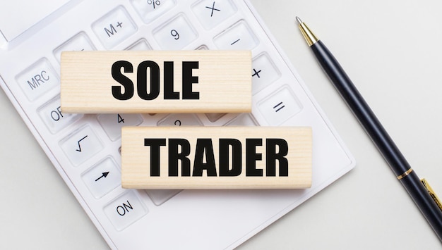 흰색 계산기의 밝은 배경에 SOLE TRADER Iie가 있는 나무 블록 Nearby는 검은색 손잡이 비즈니스 개념입니다.