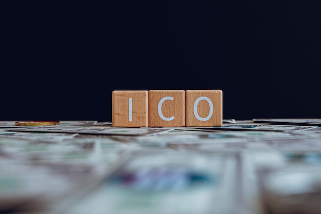 Photo wooden blocks with the text ico on a black background and crypto banknotes scattered on the ground