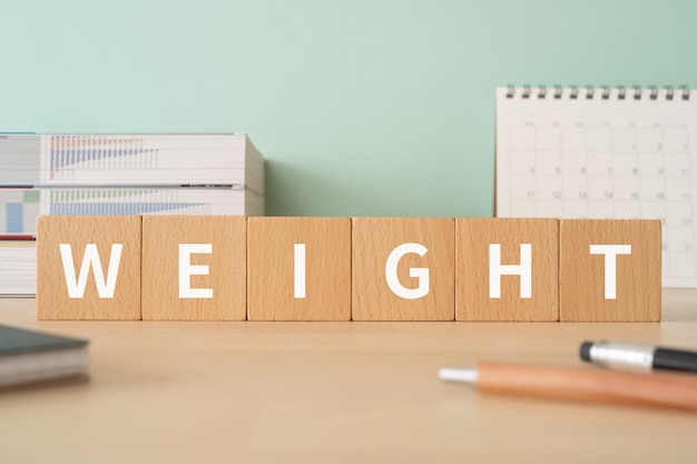 概念、ペン、ノート、および書籍の WEIGHT テキスト付きの木製ブロック。