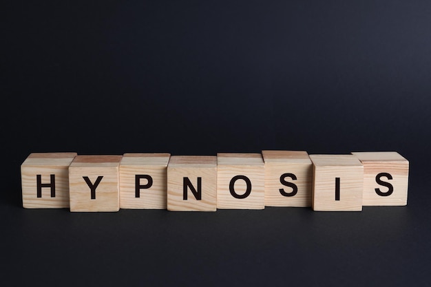 Photo wooden blocks with word hypnosis on black background