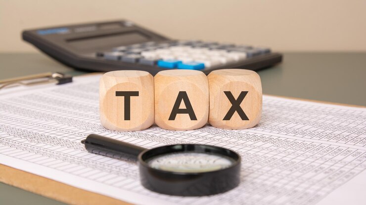 Wooden blocks with word TAX on spreadsheet with magnifier and calculator in background