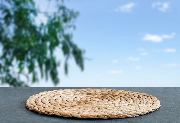 Wooden blue tabletop with napkin and free space for installing a product or layout on a background of blue sky with clouds and green tree