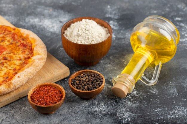 Wooden board of cheesy pizza and various condiments on stone background. 