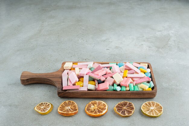 Wooden board of colorful bubble gums and lemon slices on stone.