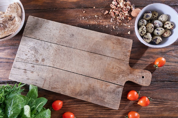 Wooden board on the kitchen table around boiled quail eggs in a bowl, pieces of nuts, tomatoes, meat and greens. Copy space. Ingredients for Healthy Salad. Flat lay
