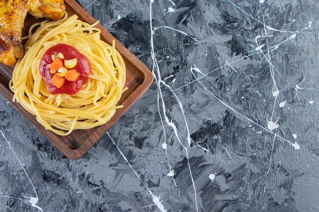 Wooden board of noodles with fried chicken wings on marble surface. 