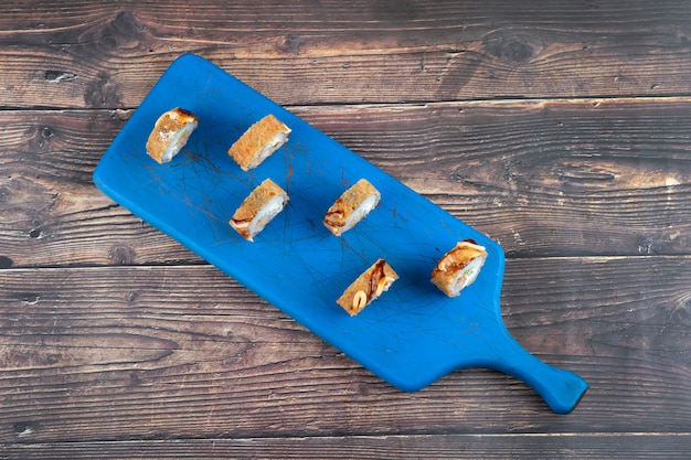 A wooden board of sushi rolls with shrimp, avocado, cheese, omelet breading . 