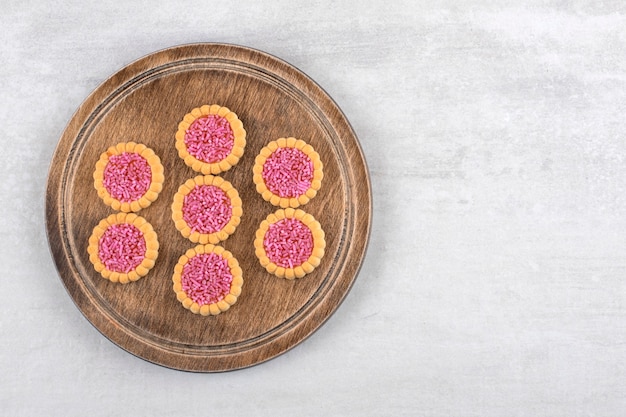 A wooden board of sweet cookies with sprinkles in hole on a stone background.