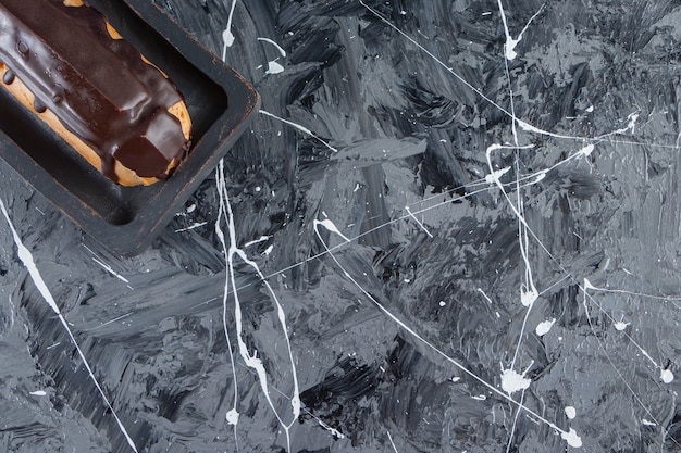 A wooden board of tasty chocolate eclair placed on a marble background. 