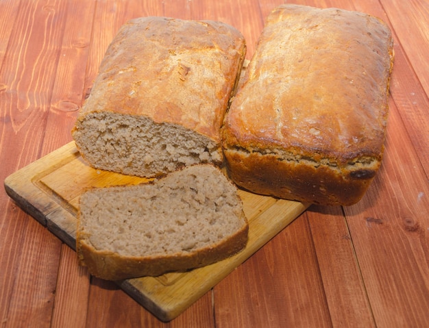 On a wooden Board two loaves of fresh bread with a piece.