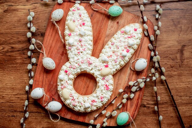 A wooden board with a bunny shaped cookie with easter eggs on it.